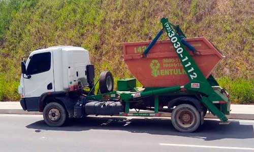 Caminhão da S.A. Entulho carregando uma caçamba laranja na via, em Manaus.